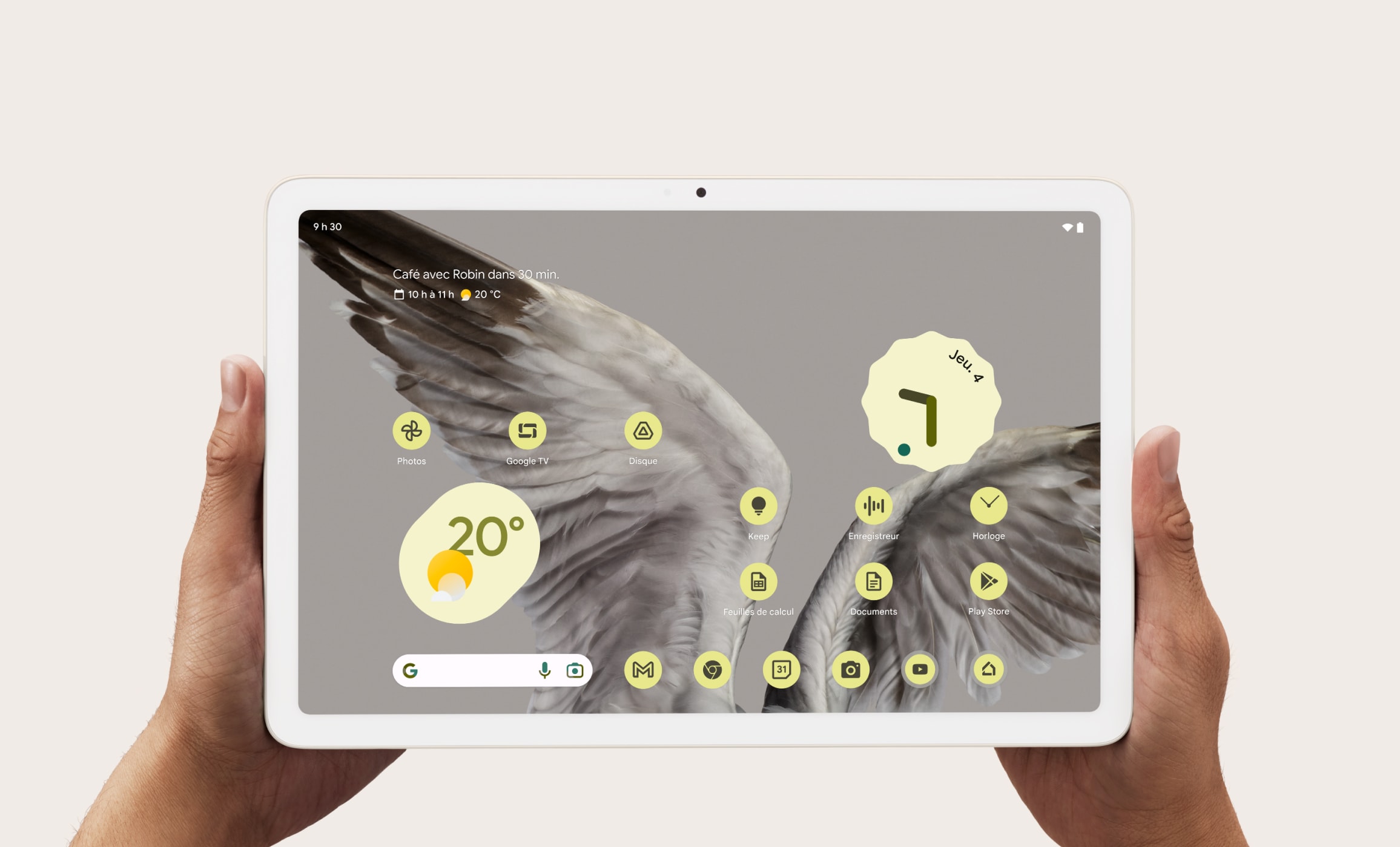 Deux mains tenant la Pixel Tablet avec la météo et l'heure affichées sur l'écran frontal.