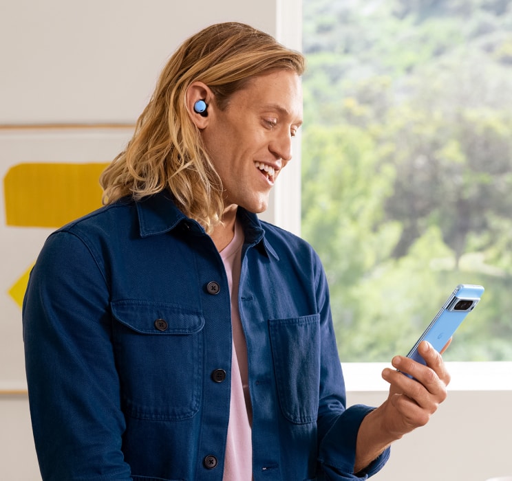 A person smiles at their Pixel 8 while using their Pixel Buds to talk on the phone.