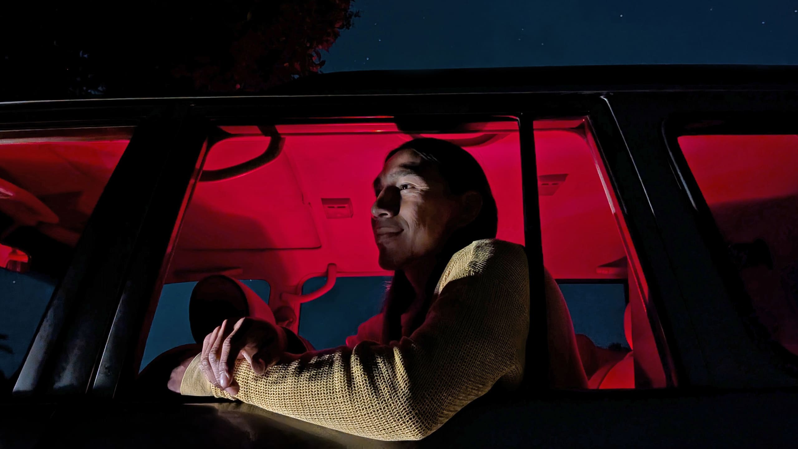 A person sits in a car during the night. The interior glows red.